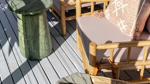 Une terrasse en bois avec une chaise et un tabouret en osier.