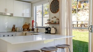 Une cuisine moderne avec des meubles blancs, un îlot central doté de tabourets, une horloge et une vue sur un jardin arrière avec une terrasse.