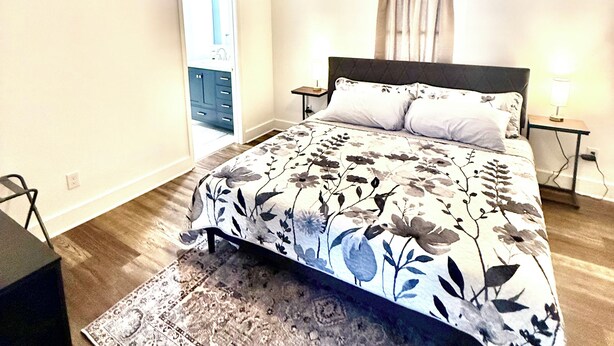 A bedroom with a bed, a ceiling fan, a nightstand with a lamp, a window with curtains, and a door leading to another room. - Beautiful modern renovated 4 bedroom and 4.5 bath within a block of HPU (High Point)