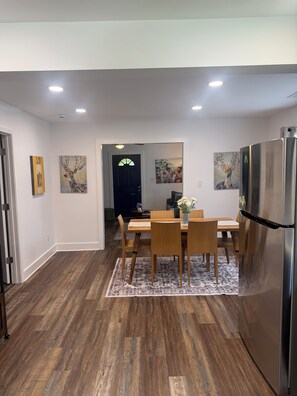 Cocina moderna con zona de comedor, que incluye una mesa de madera, sillas, un refrigerador y obras de arte en las paredes.