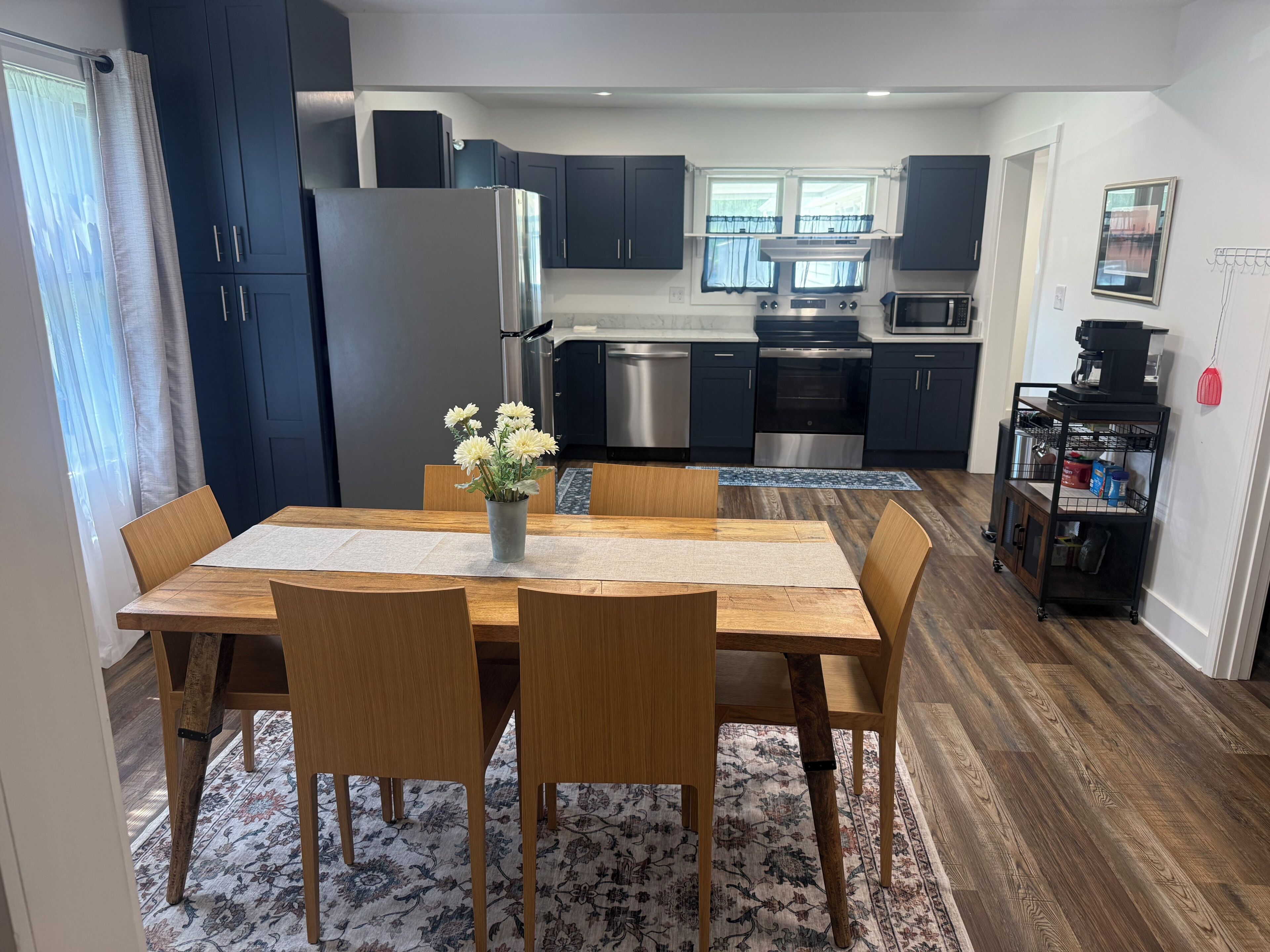 Una cocina moderna con armarios oscuros, electrodomésticos de acero inoxidable y una zona de comedor con una mesa y sillas de madera.