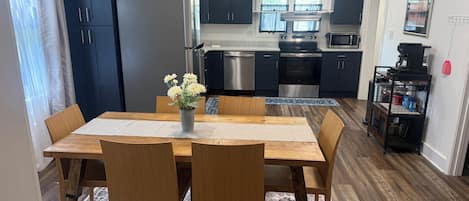 Una cocina moderna con armarios oscuros, electrodomésticos de acero inoxidable y una zona de comedor con una mesa y sillas de madera.