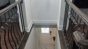Una escala amb graons de fusta i baranes metàl·liques negres que condueix a una habitació amb una porta blanca i una finestra.