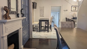Una cuina moderna amb una llar de foc, una zona de menjador amb una taula gran i caires, i una sala d'estar amb televisió i objectes decoratius.