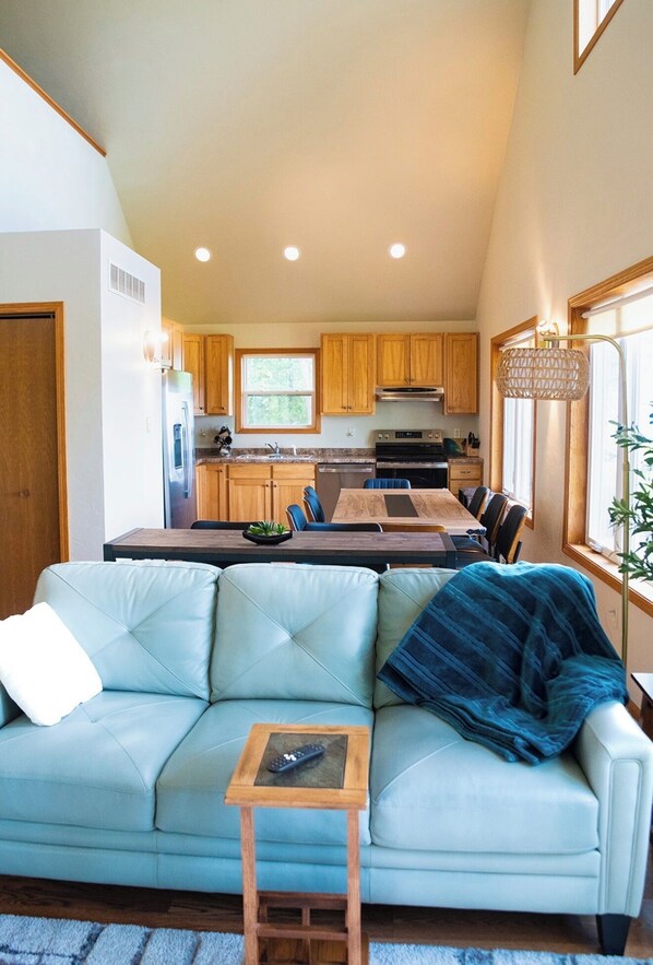 A modern kitchen with wooden cabinets, a dining area with a table and chairs, and a living room with a sofa and a small table.