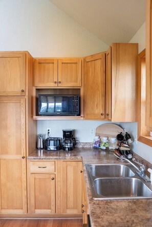 A compact kitchen with wooden cabinets, a microwave, a coffee maker, a toaster, and a sink.