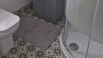 Et badeværelse med toilet, vask med spejl, brusebad og gulvfliser med mønster.