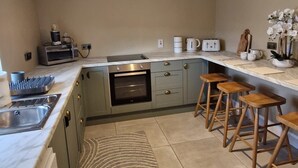 A modern kitchen with a built-in oven, a microwave, a coffee maker, and a toaster. There are wooden stools and a patterned rug. - Peaceful 2-bedroom house in DL perfect for relaxing getaways (DL)