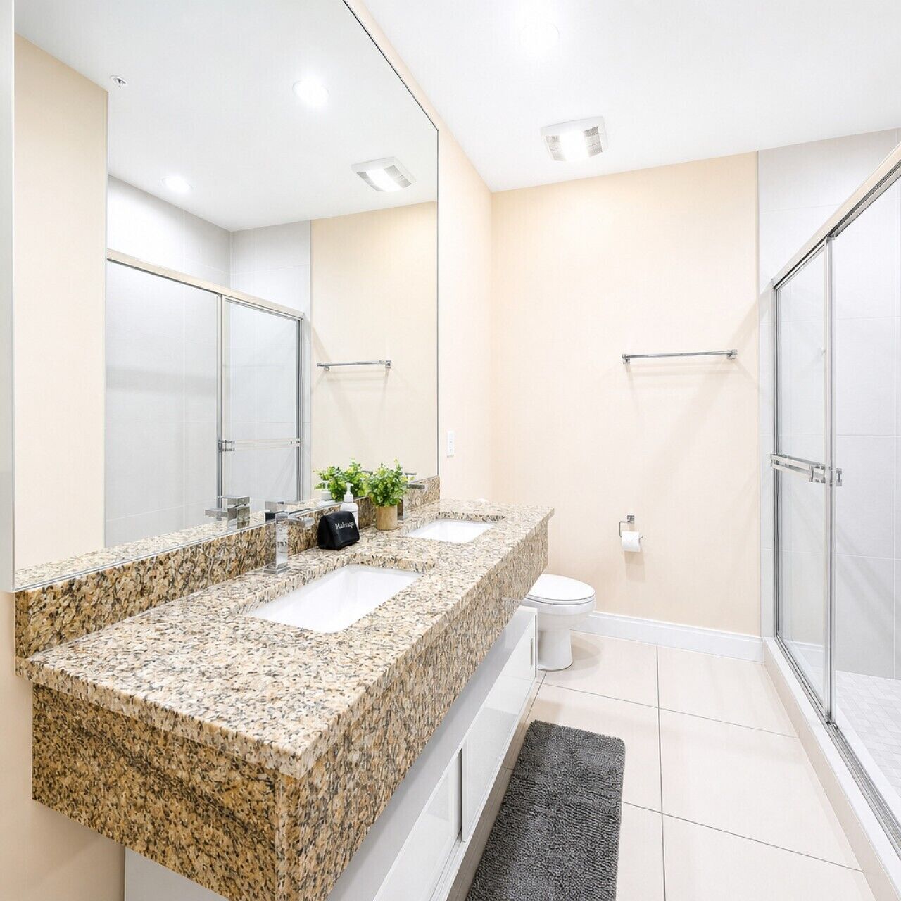 A modern bathroom with a granite countertop, a toilet, a shower, and a large mirror.