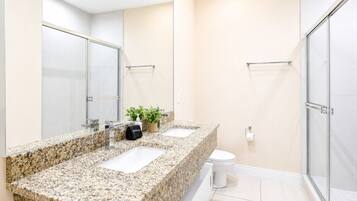 A modern bathroom with a granite countertop, a toilet, a shower, and a large mirror.