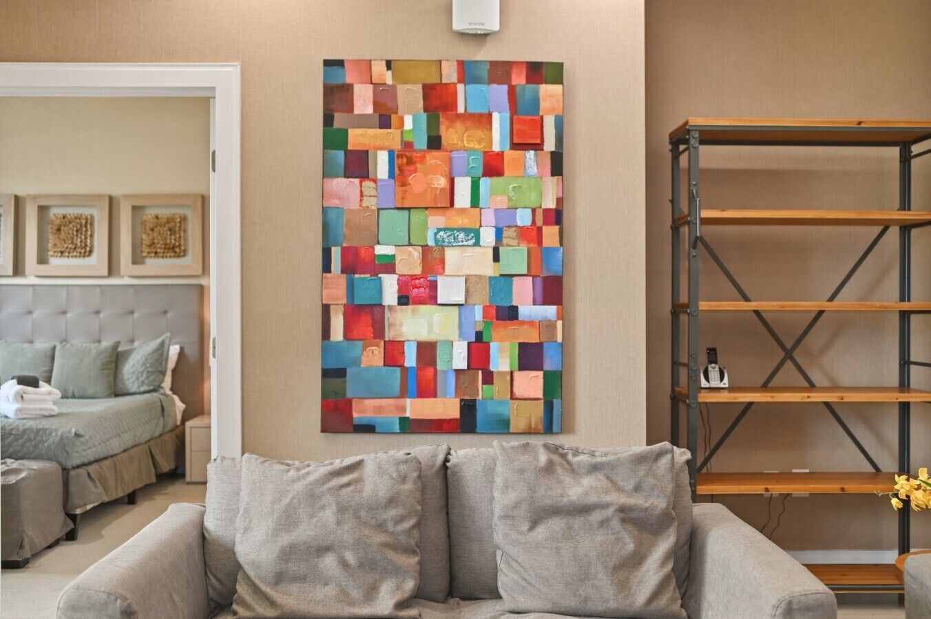 A living room with a grey sofa, a colorful abstract painting, and a wooden shelving unit.