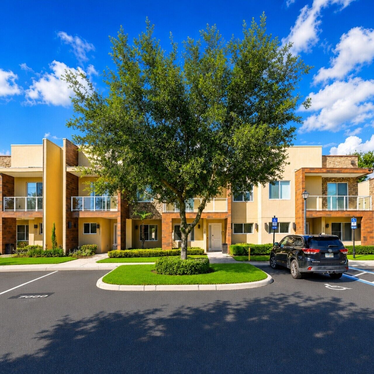A multi-story hotel with a central courtyard, a tree, and a parking area.