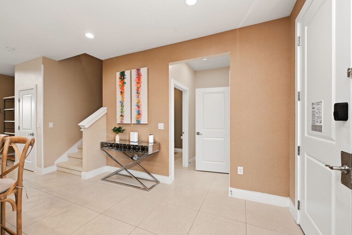A hallway with beige walls, white doors, a staircase, and a metal-framed table with a plant.