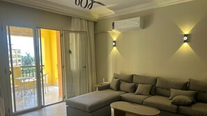 A living room with a sectional sofa, a coffee table, and a sliding glass door leading to an outdoor area. - Modern 2-bedroom Apt | Dreamland Golf & Pool View (Giza Governorate)
