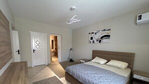 A bedroom with a bed, bedside tables, a vacuum cleaner, a door, and a ceiling light fixture. - Modern 2-bedroom Apt | Dreamland Golf & Pool View (Giza Governorate)