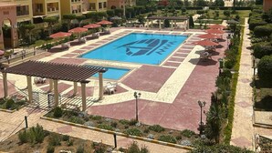 A hotel with a swimming pool, outdoor seating, and a garden area. - Modern 2-bedroom Apt | Dreamland Golf & Pool View (Giza Governorate)