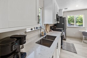 Una cocina moderna con armarios blancos, un lavamanos doble, una cafetera y vistas al exterior a través de una ventana.