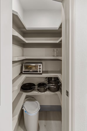 Cocina compacta con horno tostador integrado, un cubo de basura y un estante pequeño con utensilios de cocina.