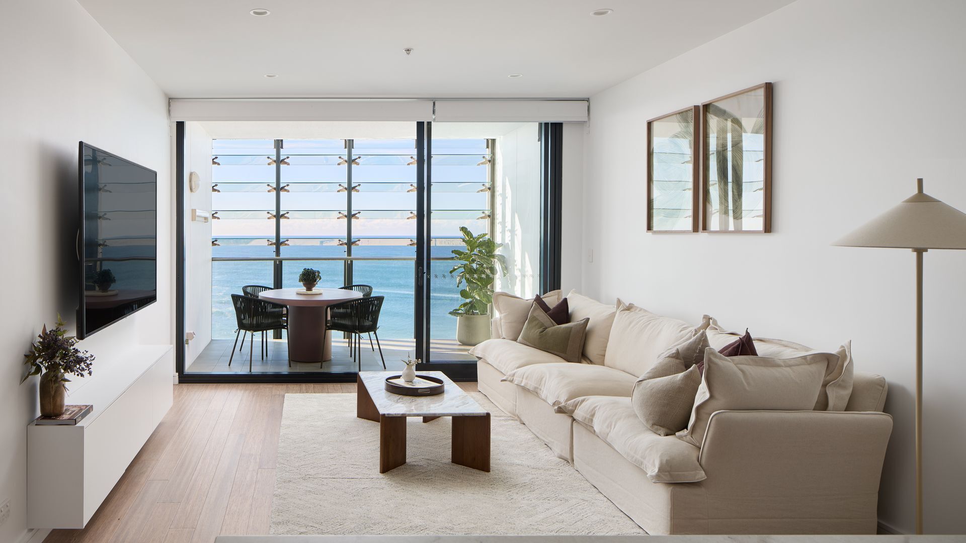 A modern living room with a balcony, a flat-screen TV, a sofa, and a dining table.