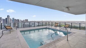 Una piscina sul tetto con vista sulla città, lettini e un soffitto in cemento.