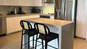 Una cucina moderna con mobili bianchi, un frigorifero in acciaio inossidabile, un forno a microonde e due sgabelli neri.