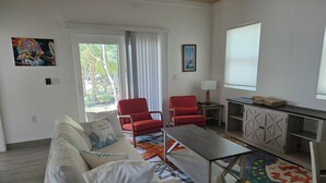 Ein Wohnzimmer mit einer Couch, zwei roten Sesseln, einem Couchtisch, einer Lampe und Blick durch ein Fenster.