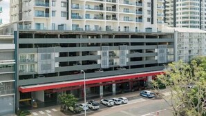 Un edifici residencial de diverses plantes amb balcons, un aparcament i un cel serè.