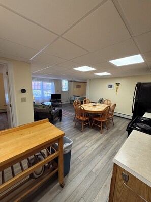 Ein Zimmer mit Esstisch, Stühlen, Herd, Mülleimer und Fernseher.