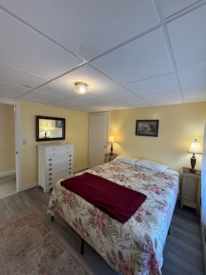 A bedroom with a bed, dresser, nightstands, lamps, and a ceiling light fixture. - Beachfront 2-Bedroom Apartment on Wells Beach Sleeps 6 (Wells)