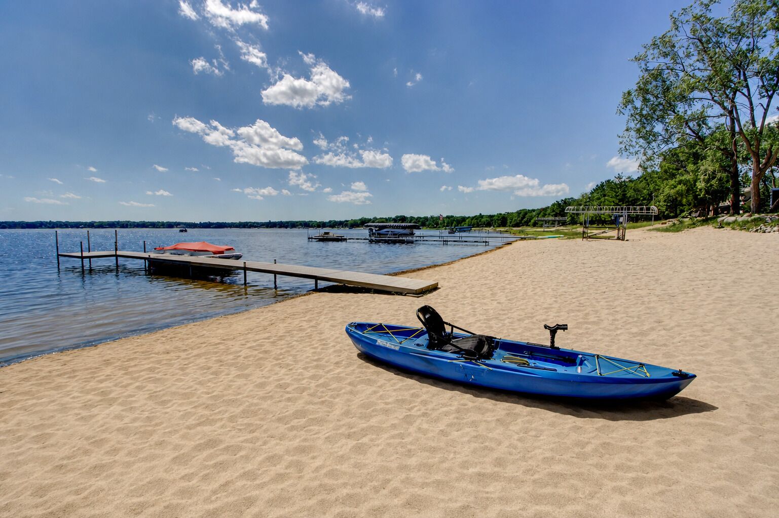 Ein sandiger Strand mit einem blauen Kajak und einem roten Boot, die an einer Holzsteganlage liegen.