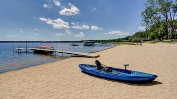 Ein sandiger Strand mit einem blauen Kajak und einem roten Boot, die an einer Holzsteganlage liegen.