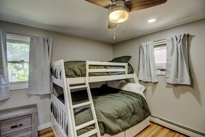 A bunk bed room with a ceiling fan, a window with curtains, and a radiator.