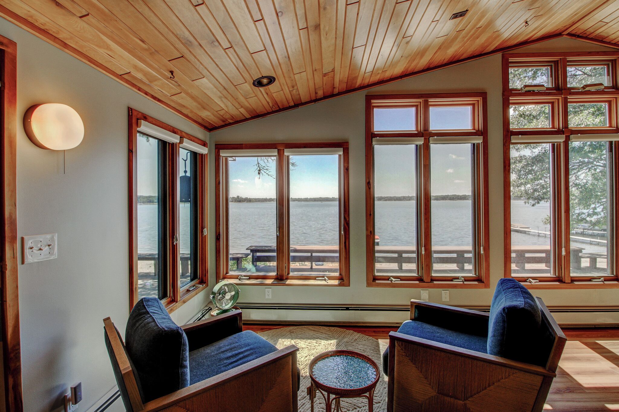 Ein Zimmer mit großen Fenstern und Blick auf ein Gewässer, Holzboden und zwei Stühle mit Kissen.