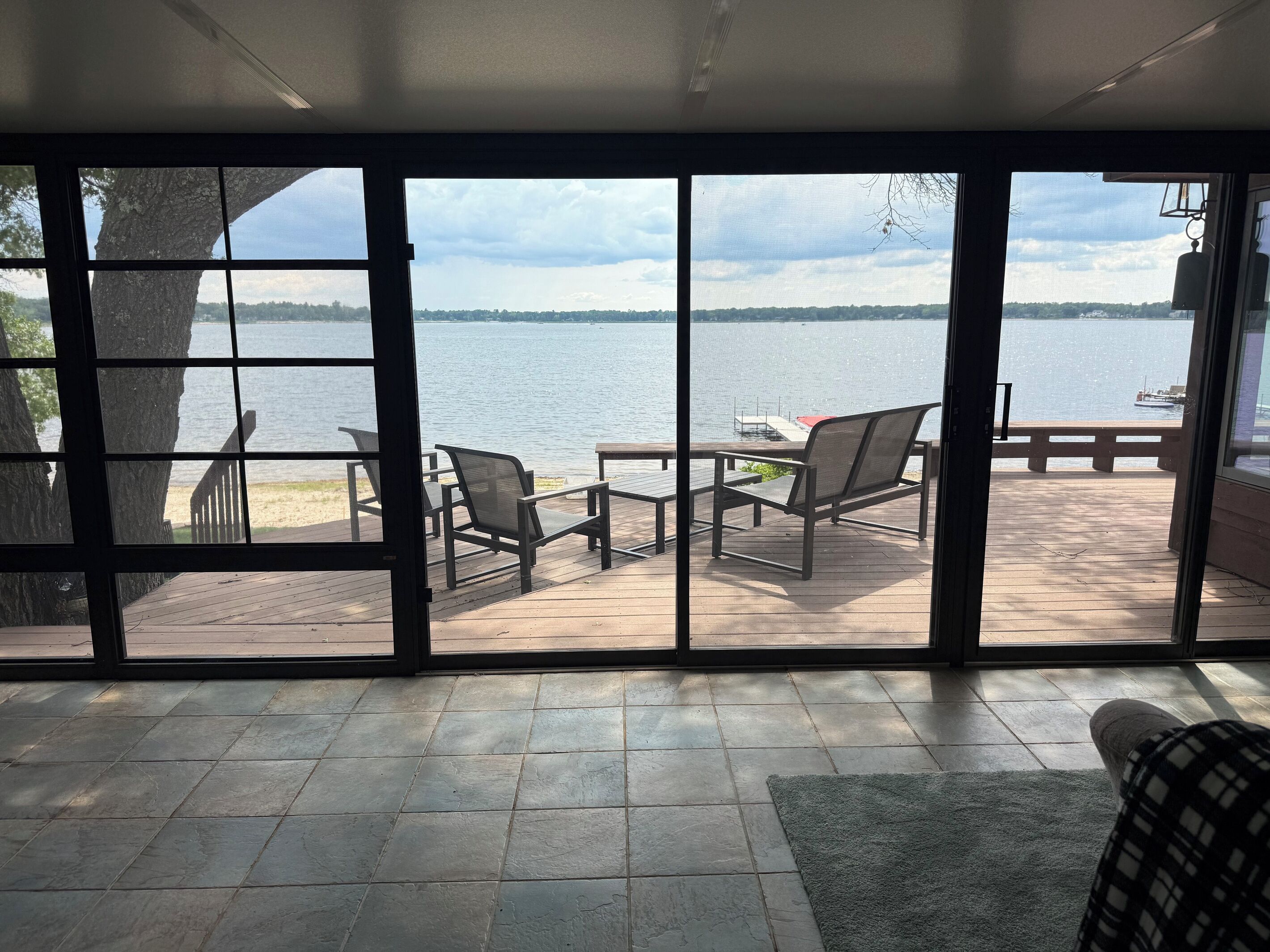 A room with a large window overlooking a deck with outdoor furniture and a view of a lake.