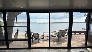 Ein Zimmer mit großem Fenster, das auf eine Terrasse mit Gartenmöbeln und einen Seeblick blickt.