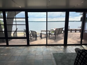 A room with a large window overlooking a deck with outdoor furniture and a view of a lake.