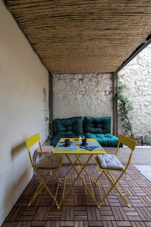 A covered patio with a table and chairs, a cushioned sofa, and a stone wall. - Fully renovated one bedroom brand new apt.in the heart of Athens (Athina)