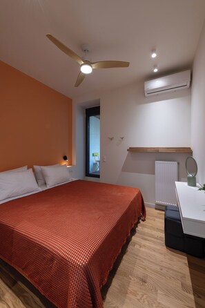 Ein Schlafzimmer mit Bett, Deckenventilator, Klimaanlage, Fenster mit Jalousien, Heizkörper und Nachttisch mit Lampe.