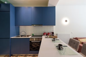 A modern kitchen with blue cabinets, a white countertop, and a dining area with a table and chairs. - Fully renovated one bedroom brand new apt.in the heart of Athens (Athina)