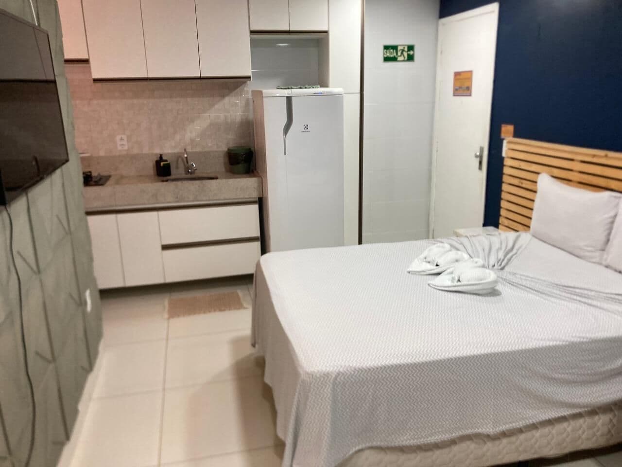 Une chambre d’hôtel équipée d’un lit, d’une petite kitchenette, d’un réfrigérateur et d’une porte avec une pancarte.