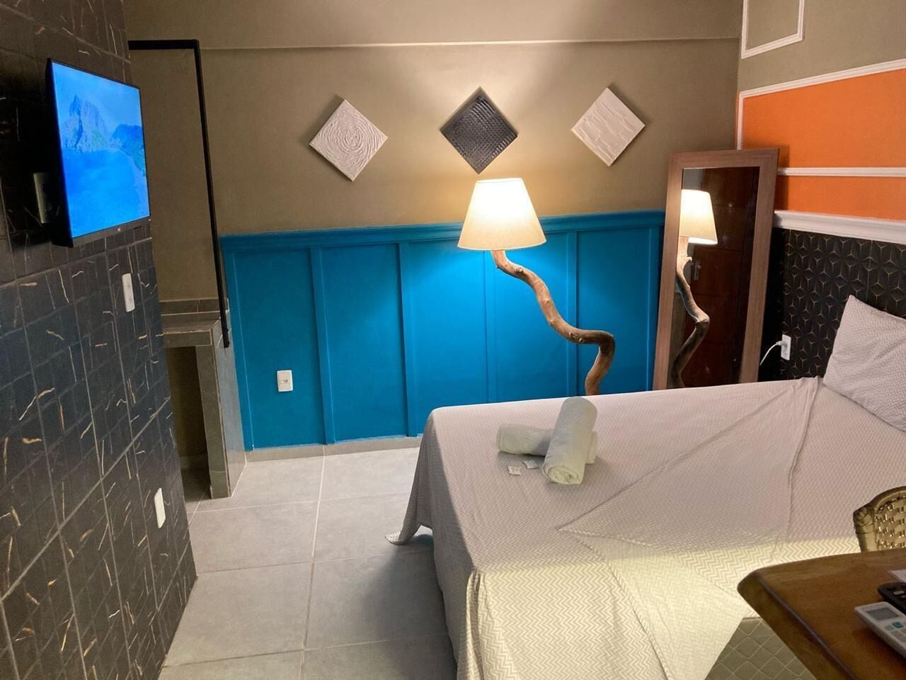 Habitación de hotel con una cama, un televisor, una lámpara de pared y una pared de acento azul.