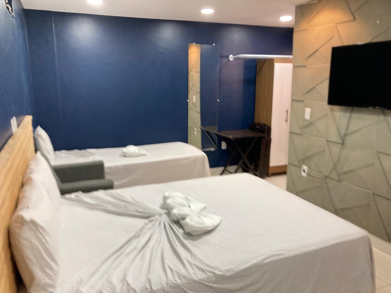 Una habitación de hotel con dos camas, un televisor montado en la pared y una mesita.