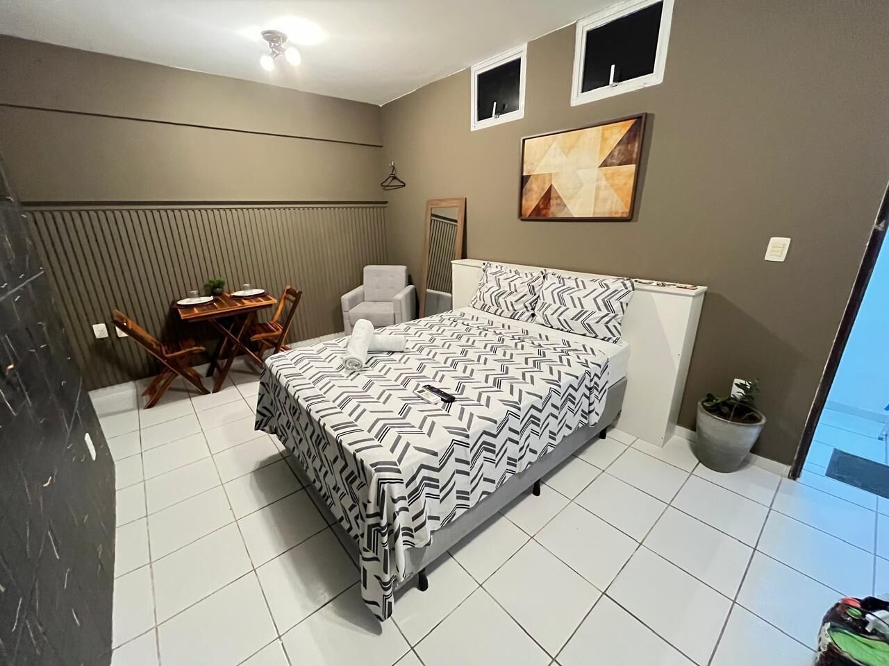 A bedroom with a bed, a chair, a table, and a potted plant.