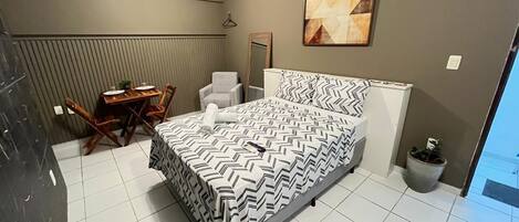 A bedroom with a bed, a chair, a table, and a potted plant.