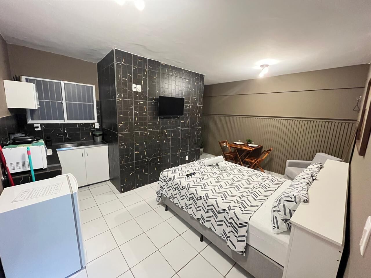 A compact hotel room with a bed, a small kitchenette, a seating area, and a TV.