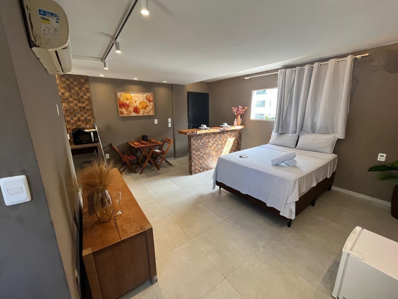 Ein Schlafzimmer mit Bett, Schreibtisch, Stuhl, Fernseher und einem kleinen Tisch mit Vase und Weinglas.