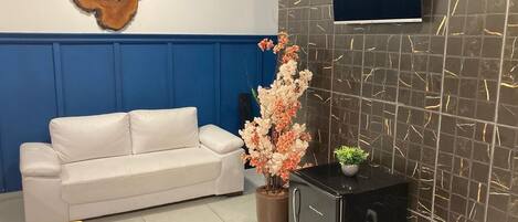 A room with a white sofa, a small black cabinet, a decorative vase with flowers, and a mounted TV on the wall.