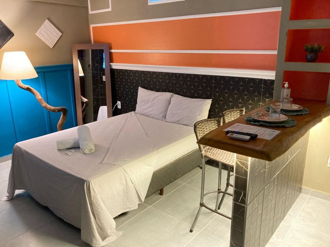 A hotel room with a bed, a small bar area, a chair, and a lamp.