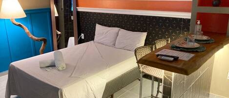 A hotel room with a bed, a small bar area, a chair, and a lamp.