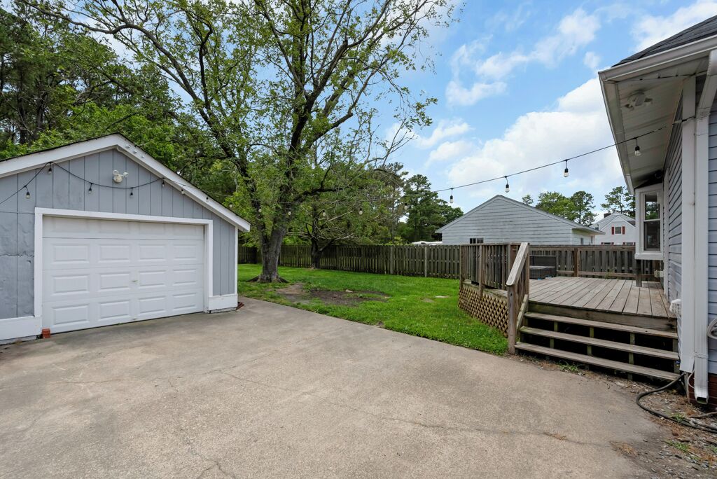 Un jardin à l’arrière d’une maison, avec un garage, une terrasse en bois et un arbre.